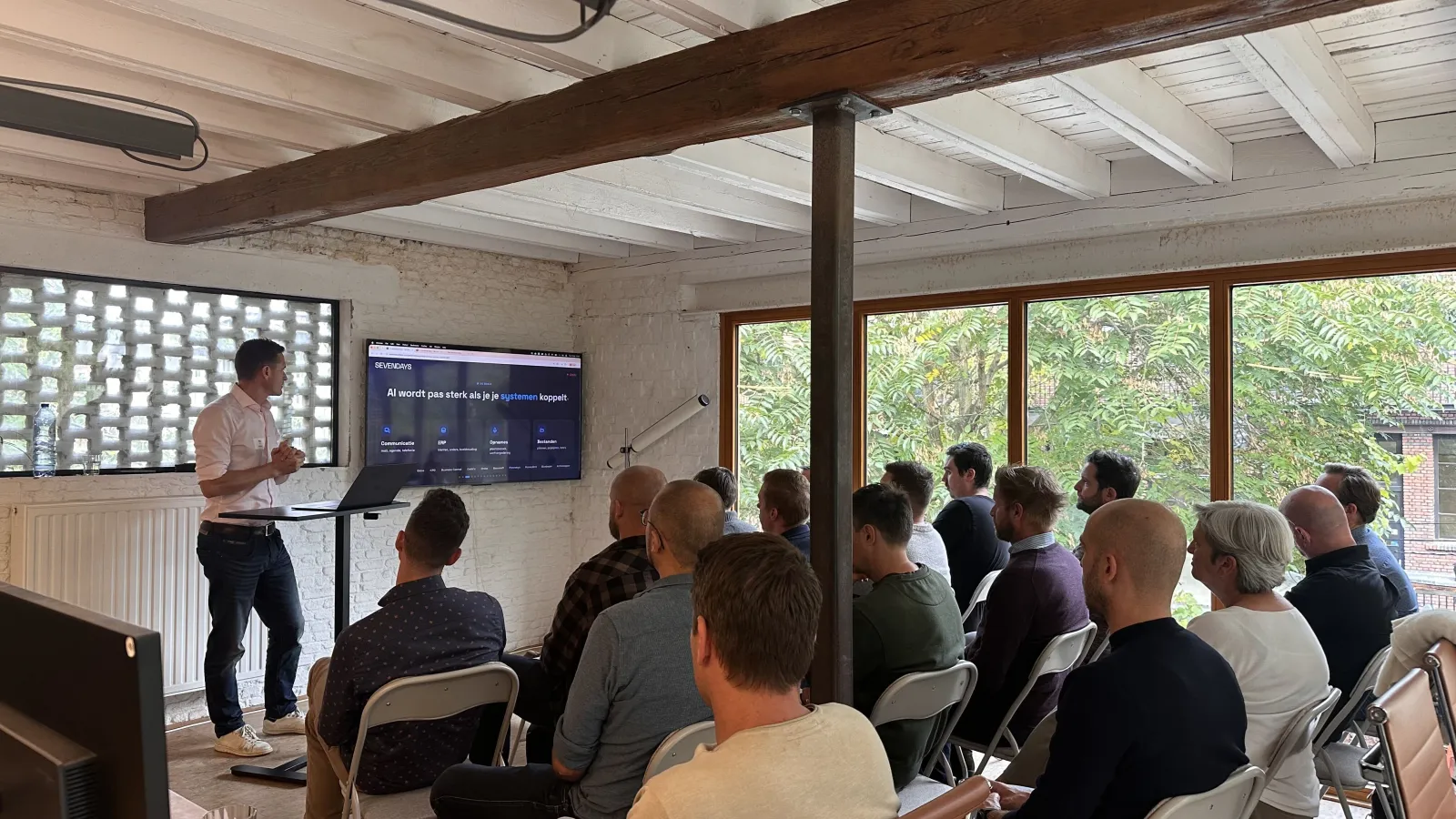 Max Acke geeft de AI-workshop voor de bouw op het Sevendays-kantoor, de zaal kijkt naar een slide over systemen koppelen