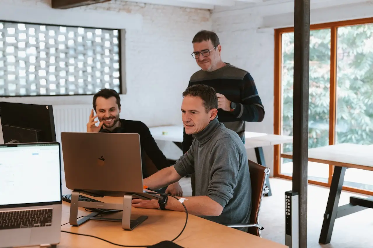 Drie collega's van Sevendays bekijken samen iets op een laptop